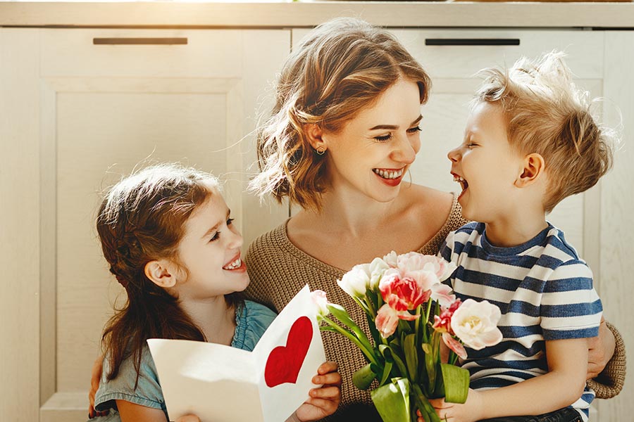 Personal Insurance - Mother Sits on the Kitchen Floor With Her Two Small Children Who Have Just Given Her Flowers and a Card