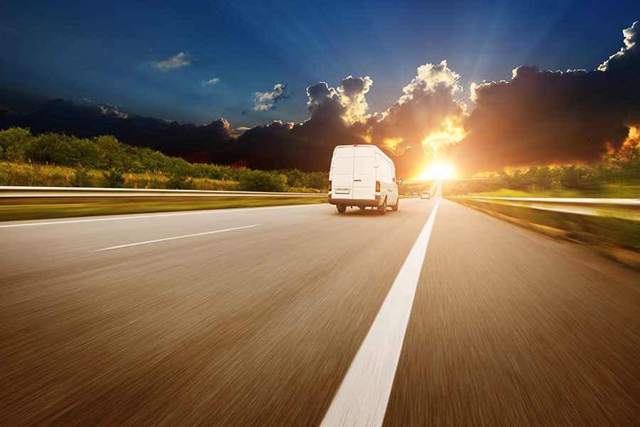 Cargo Insurance - White Cargo Van Driving Down the Road Into the Sunrise